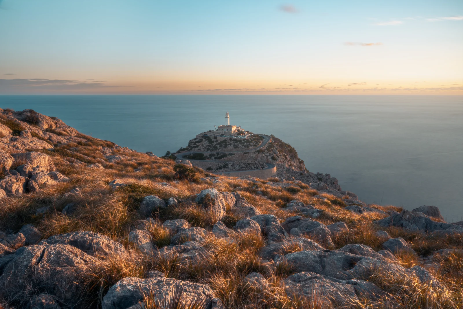 Costa rocciosa e faro sul promontorio al tramonto